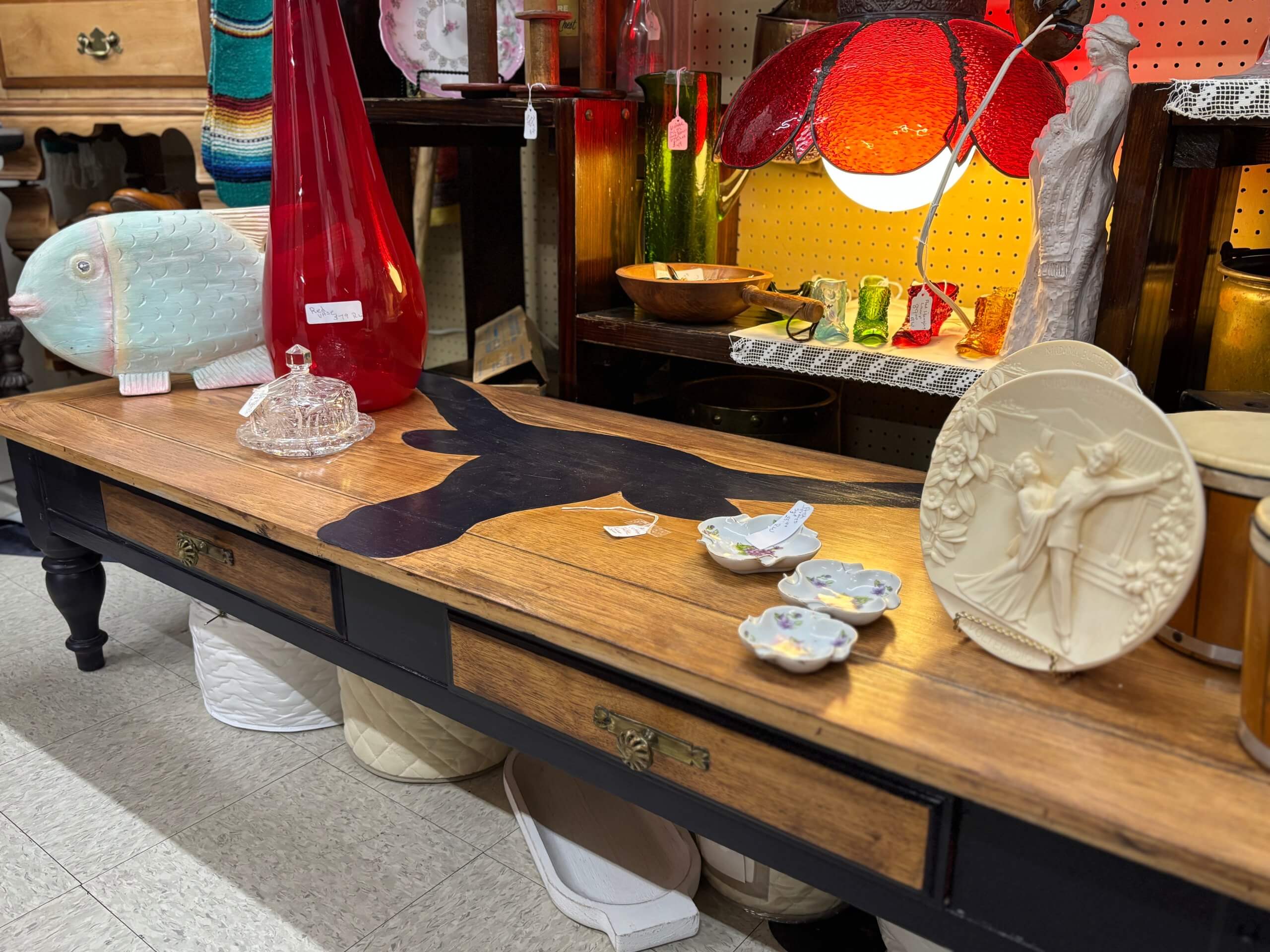 Eclectic vintage display with red glass vases, ceramic fish, decorative plate, and wood table at Elmwood Antique Centre in Abilene, TX