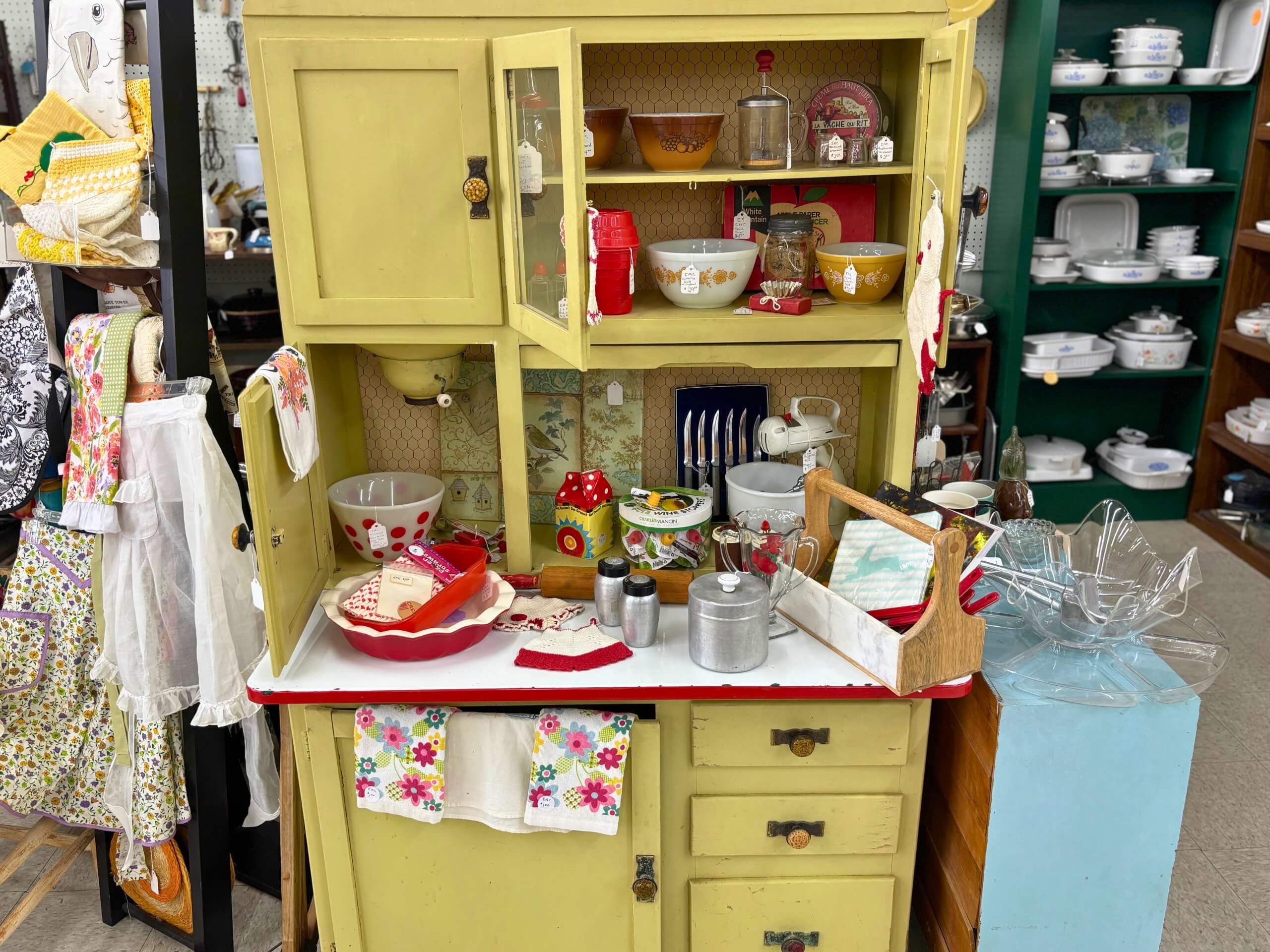 Vintage yellow kitchen hutch filled with retro bowls, utensils, and aprons at Elmwood Antique Centre in Abilene, TX